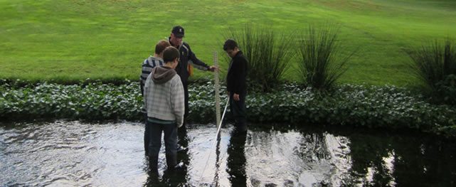 Glenwood Golf Course Superintendent Steve Kealy helps students measure water flow of a stream running through the course as part of the First Green (cortesía clearingmagazine.org)
